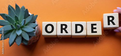 Order symbol. Wooden cubes with word Order. Businessman hand. Beautiful orange background with succulent plant. Business and Order concept. Copy space.