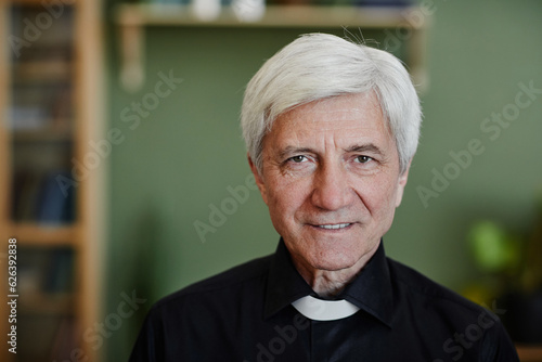 Canvas Print Close up portrait of white haired senior priest smiling at camera in office sett