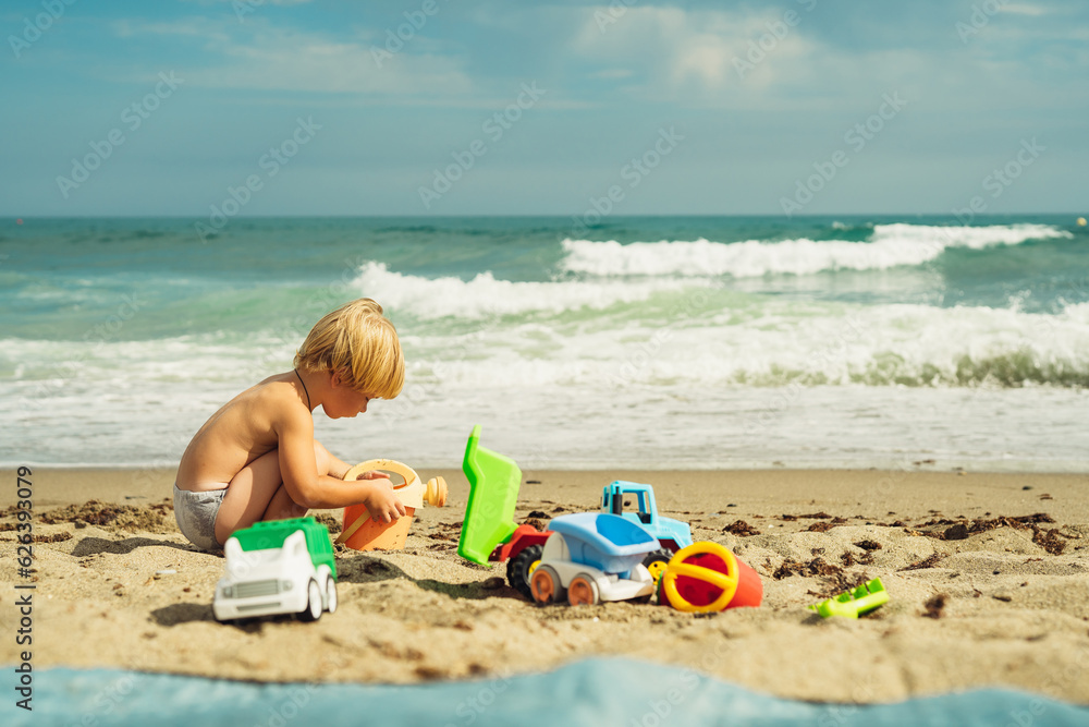 boy 3 years old blond plays on the seashore in the sand with plastic toys against the background of the sea boy 3 years old blond plays on the seashore in the sand with plastic toys against the background of the sea