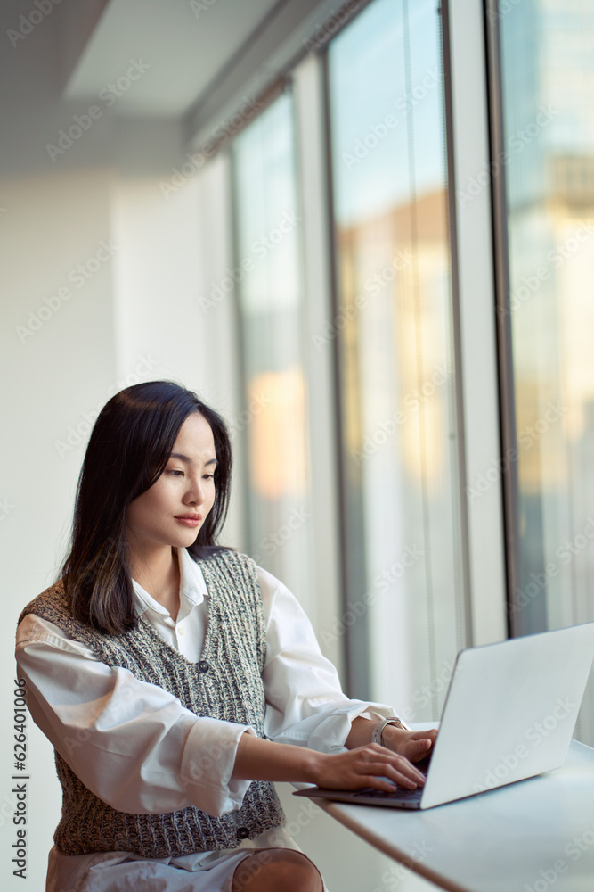 Young pretty Asian business woman employee or student working on laptop in corporate office. Professional businesswoman company worker using computer, typing, elearning sitting at desk. Vertical Young pretty Asian business woman employee or student working on laptop in corporate office. Professional businesswoman company worker using computer, typing, elearning sitting at desk. Vertical