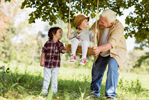 Young boy and girl using a swing in the park with their grandfather photo