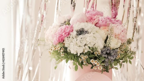 An elegant bouquet of fresh roses, peonies, and daisies in a pink box, beautifully arranged and placed by a light-filled window.