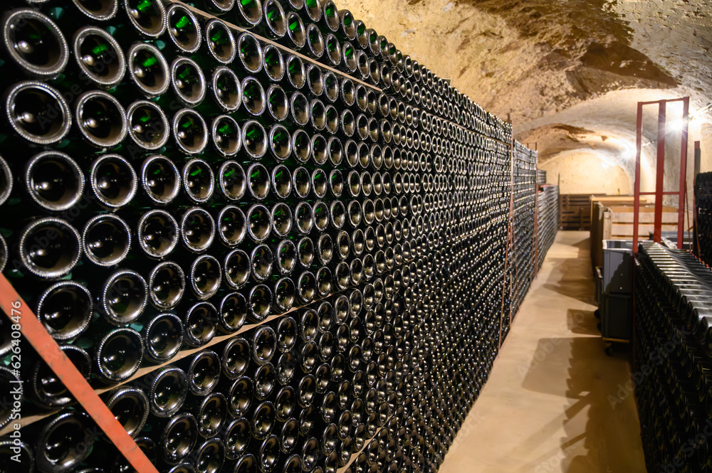 Fototapeta premium Walking in deep undergrounds caves with bottles on wooden racks, making champagne sparkling wine from chardonnay and pinor noir grapes in Epernay, Champagne, France