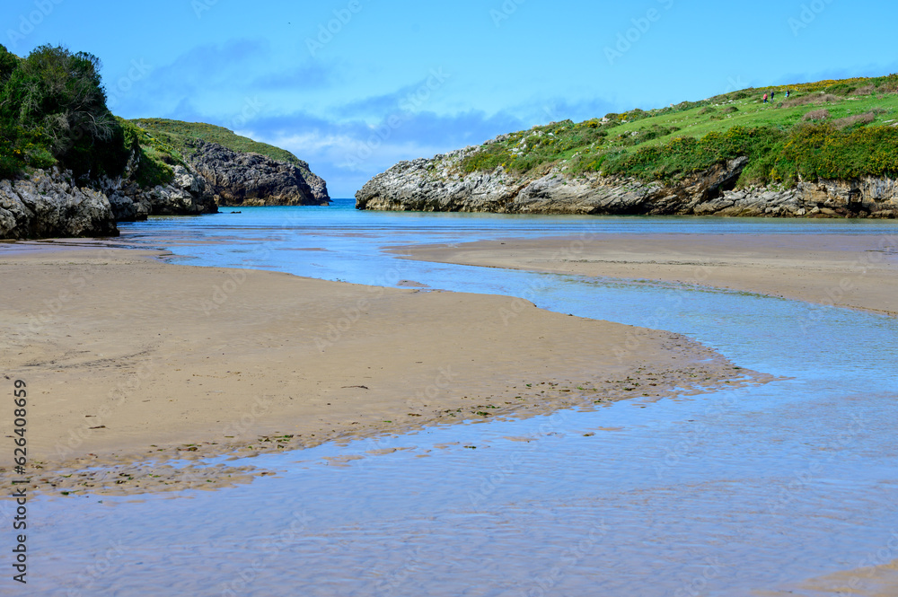 View on Playa de Poo during low tide near Llanes, Green coast of Asturias, North Spain with sandy beaches, cliffs, hidden caves, green fields and mountains.