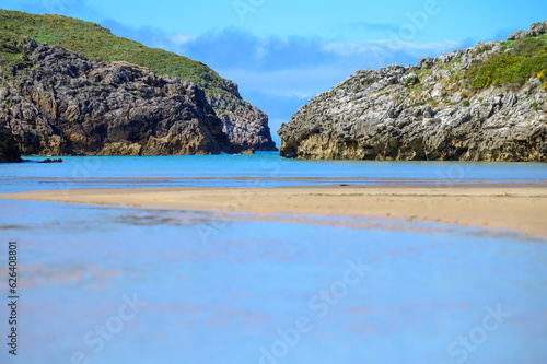 View on Playa de Poo during low tide near Llanes, Green coast of Asturias, North Spain with sandy beaches, cliffs, hidden caves, green fields and mountains.