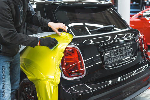 Back and truck of a car during car wrapping process at detailing station. Professional car detailer glueing yellow vehicle wrap. High quality photo