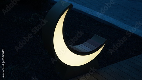 Glowing crescent lamp bench in night park photo