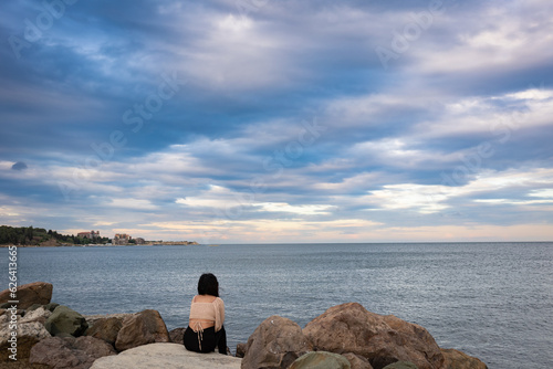 A young lady finds serenity and peace by the calm waters of the Black Sea, seated on a rock structure near the resort town of Nesebar in Southern Bulgaria.