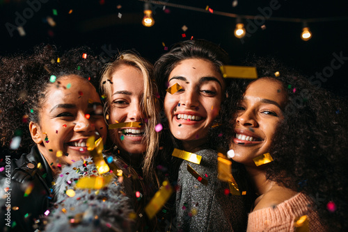 Close-up of four happy women under confetti making a selfie at night