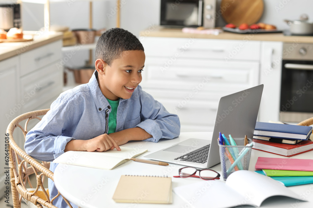 Little African-American boy studying computer sciences online in kitchen Little African-American boy studying computer sciences online in kitchen