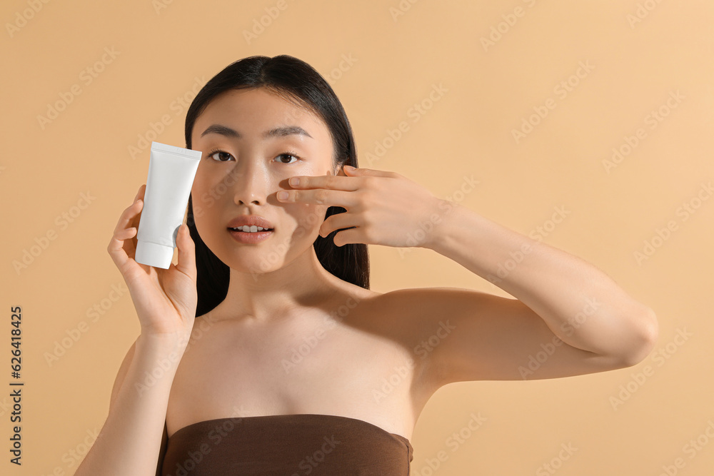 Beautiful young woman holding sun protection cream on beige background, space for text Beautiful young woman holding sun protection cream on beige background, space for text
