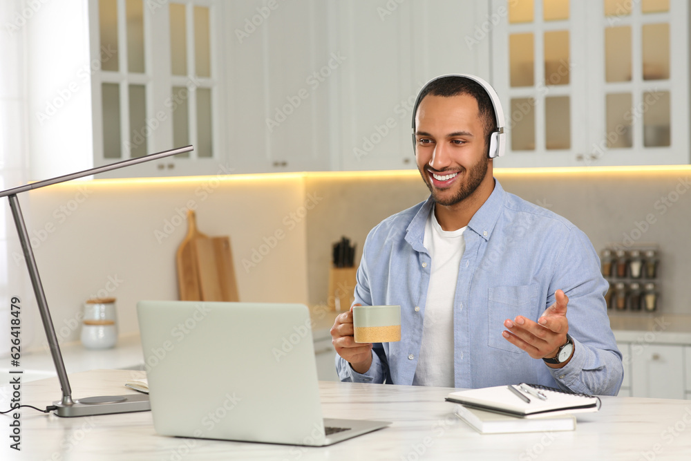 Young man with headphones having online video chat at desk in kitchen. Home office