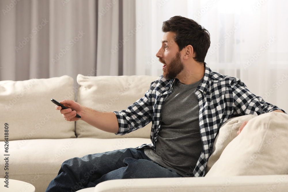 Surprised man watching TV on sofa at home