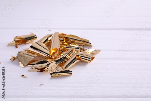 Many pieces of edible gold leaf on white wooden table, closeup. Space for text