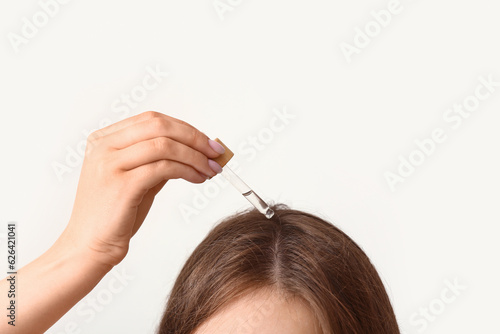 Young woman using cosmetic oil for hair treatment on light background, closeup