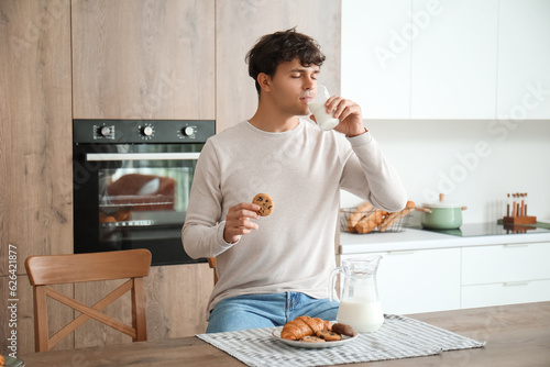 Fotografía Young man drinking fresh milk and eating cookie in kitchen