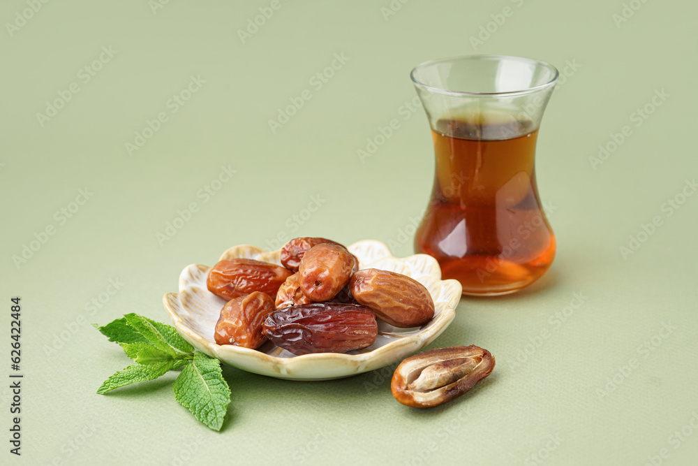 Plate with dried dates and glass of Turkish tea on green background Plate with dried dates and glass of Turkish tea on green background