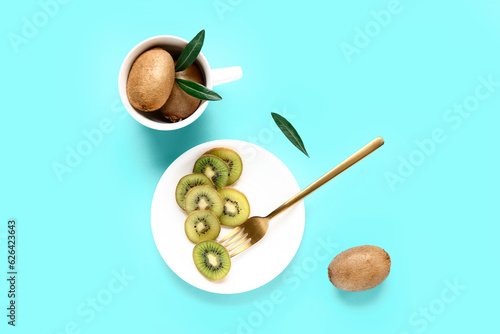 Plate and cup with fresh kiwi on turquoise background