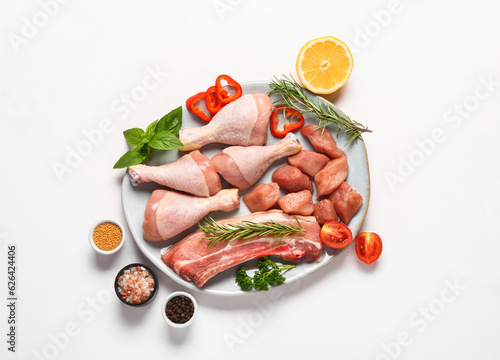 Plate with different raw meat, herbs and spices on light background