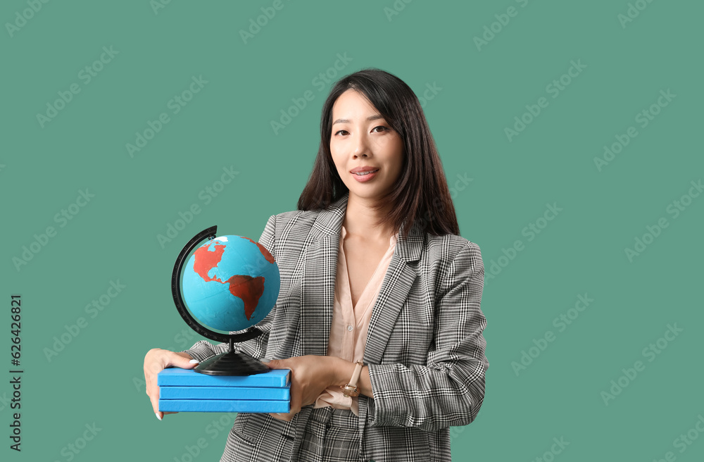 Asian Geography teacher with globe and books on green background Asian Geography teacher with globe and books on green background
