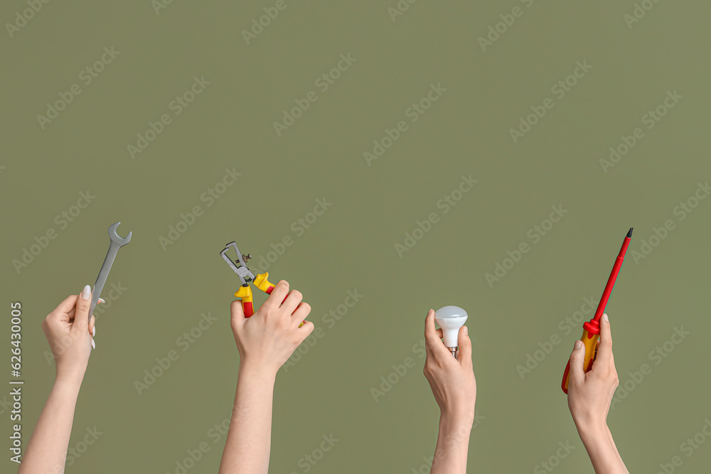 Electrician hands with light bulb and tools on green background Electrician hands with light bulb and tools on green background