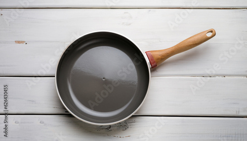 White frying pan on white rustic table. Ceramic frying pan with beautiful wooden handle.