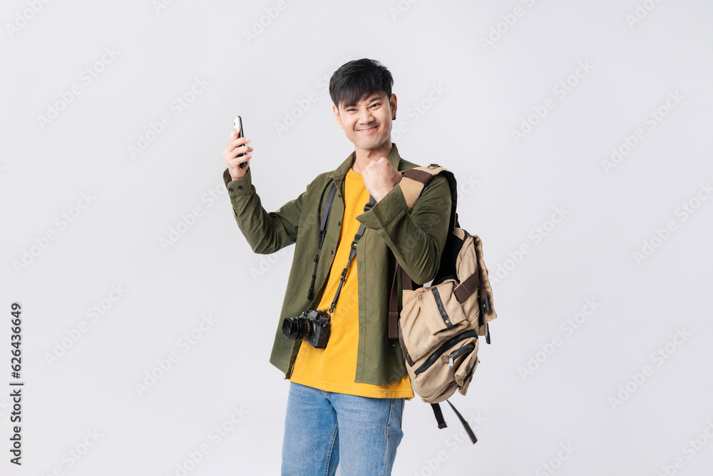 Portrait young Asian man backpacker happy smile in a casual outfit using smartphone trading or chatting or online shopping on isolated studio white background. Asian man traveller in studio shot. Portrait young Asian man backpacker happy smile in a casual outfit using smartphone trading or chatting or online shopping on isolated studio white background. Asian man traveller in studio shot.