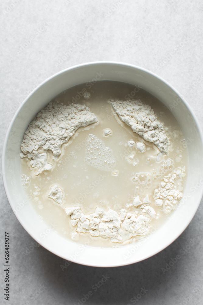 Water and flour in a white bowl, hydrating flour before baking, autolyse process of baking bread