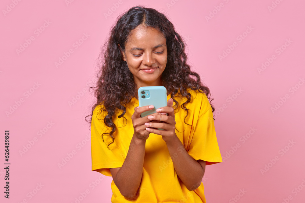 Young smiling Indian millennial woman with closed eyes holds smartphone thinking about new post for social media or personal blog stands posing on plain pink background. Chatting on phone concept Young smiling Indian millennial woman with closed eyes holds smartphone thinking about new post for social media or personal blog stands posing on plain pink background. Chatting on phone concept