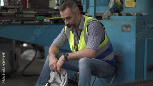 tired senior engineer worker feeling ill take a break sitting on machine in factory in . beard old male labor exhausted for hard work. depression employee burn out.