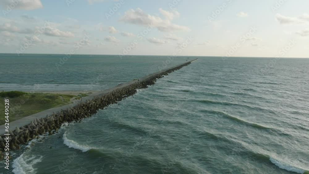 Aerial establishing view of Port of Liepaja concrete pier, Baltic sea coastline (Latvia), sunny day summer evening, golden hour light, big waves splashing, wide drone shot moving forward Aerial establishing view of Port of Liepaja concrete pier, Baltic sea coastline (Latvia), sunny day summer evening, golden hour light, big waves splashing, wide drone shot moving forward