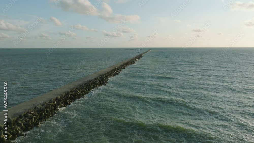 Aerial establishing view of Port of Liepaja concrete pier, Baltic sea coastline (Latvia), sunny day summer evening, golden hour light, big waves splashing, wide drone dolly shot moving right Aerial establishing view of Port of Liepaja concrete pier, Baltic sea coastline (Latvia), sunny day summer evening, golden hour light, big waves splashing, wide drone dolly shot moving right