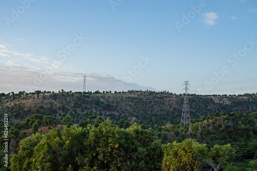 Landscape of hill with High voltage poles standing in a field under a blue sky, electric transmission. The photo is suitable to use for electricity transmission background and content media.