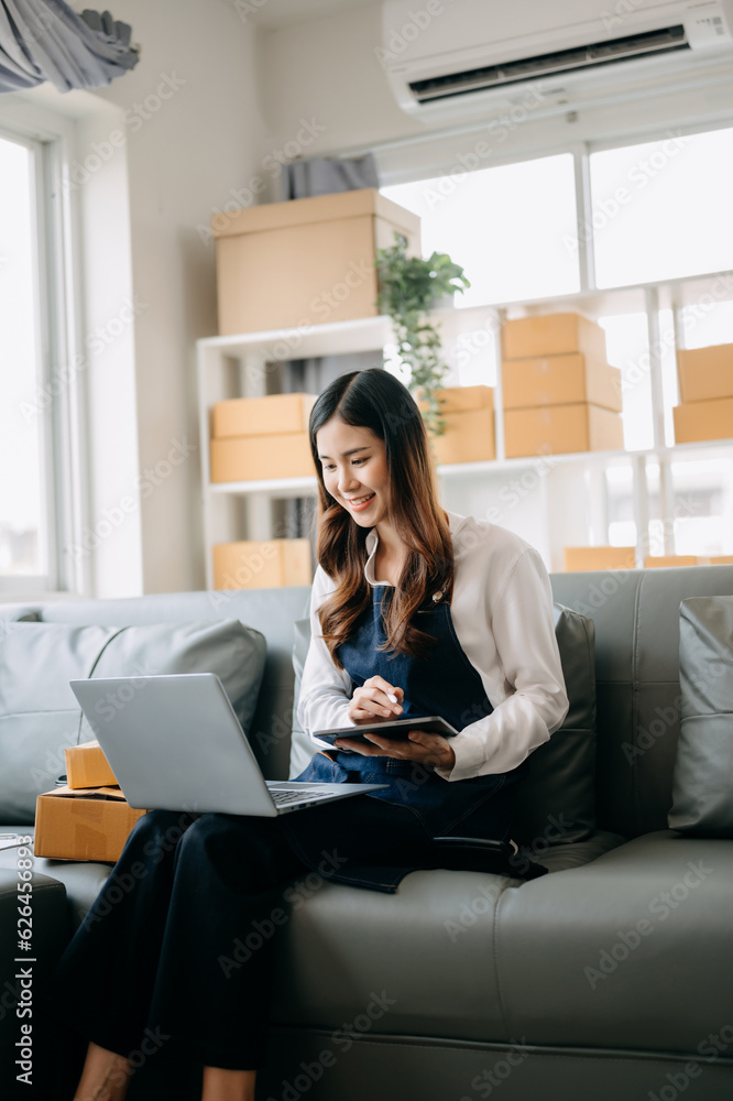 Young asian business owner woman prepare parcel box and standing check online orders for deliver to customer on tablet, laptop Shopping Online concept.. Young asian business owner woman prepare parcel box and standing check online orders for deliver to customer on tablet, laptop Shopping Online concept..