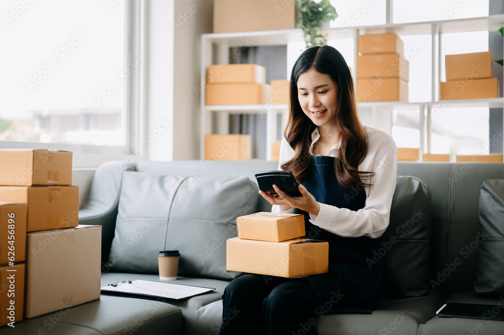 Young asian business owner woman prepare parcel box and standing check online orders for deliver to customer on tablet, laptop Shopping Online concept.. Young asian business owner woman prepare parcel box and standing check online orders for deliver to customer on tablet, laptop Shopping Online concept..