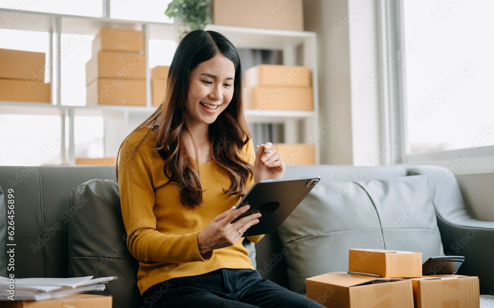Young asian business owner woman prepare parcel box and standing check online orders for deliver to customer on tablet, laptop Shopping Online concept.. Young asian business owner woman prepare parcel box and standing check online orders for deliver to customer on tablet, laptop Shopping Online concept..