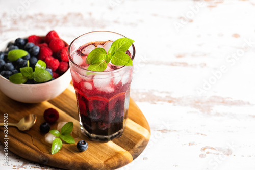 The glass of iced tea with berries on the wooden table. Cuba Libre or long island cocktail, cold drink or lemonade with fruits and basil