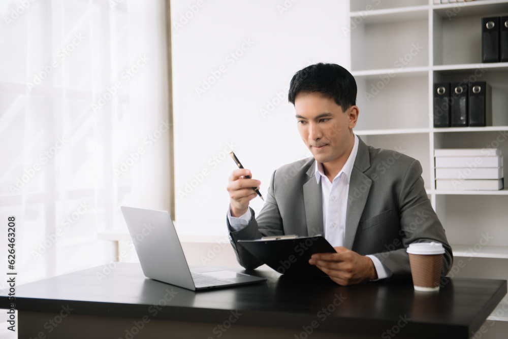 Young Asian business man using laptop and tablet while sitting at her working place. Concentrated at work. Young Asian business man using laptop and tablet while sitting at her working place. Concentrated at work.