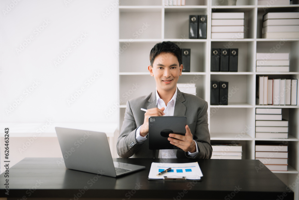 Confident Asian man with a smile standing holding notepad and tablet at the modern office. Confident Asian man with a smile standing holding notepad and tablet at the modern office.