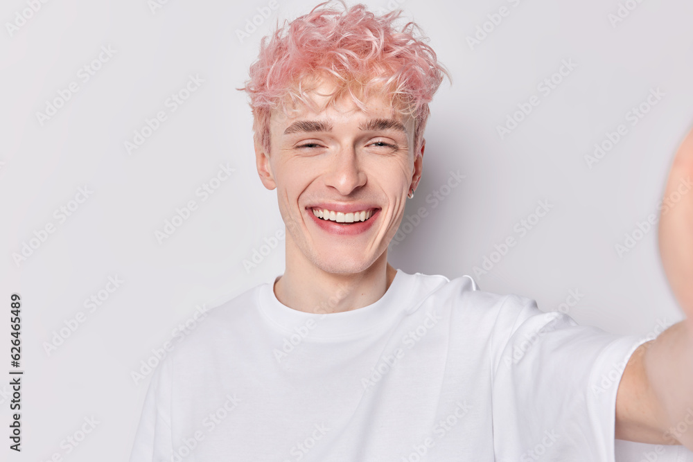 Happy young smiling broadly pink haired gender fluid European male standing isolated on white background wearing casual tshirt belongs to lg by society making selfie or taking photo keeps good shape Happy young smiling broadly pink haired gender fluid European male standing isolated on white background wearing casual tshirt belongs to lg by society making selfie or taking photo keeps good shape