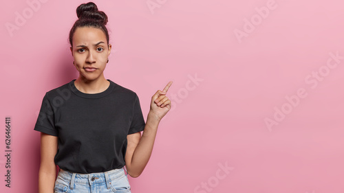 Photographie Serious displeased Latin woman with hair bun raises eyebrows looks attentively a
