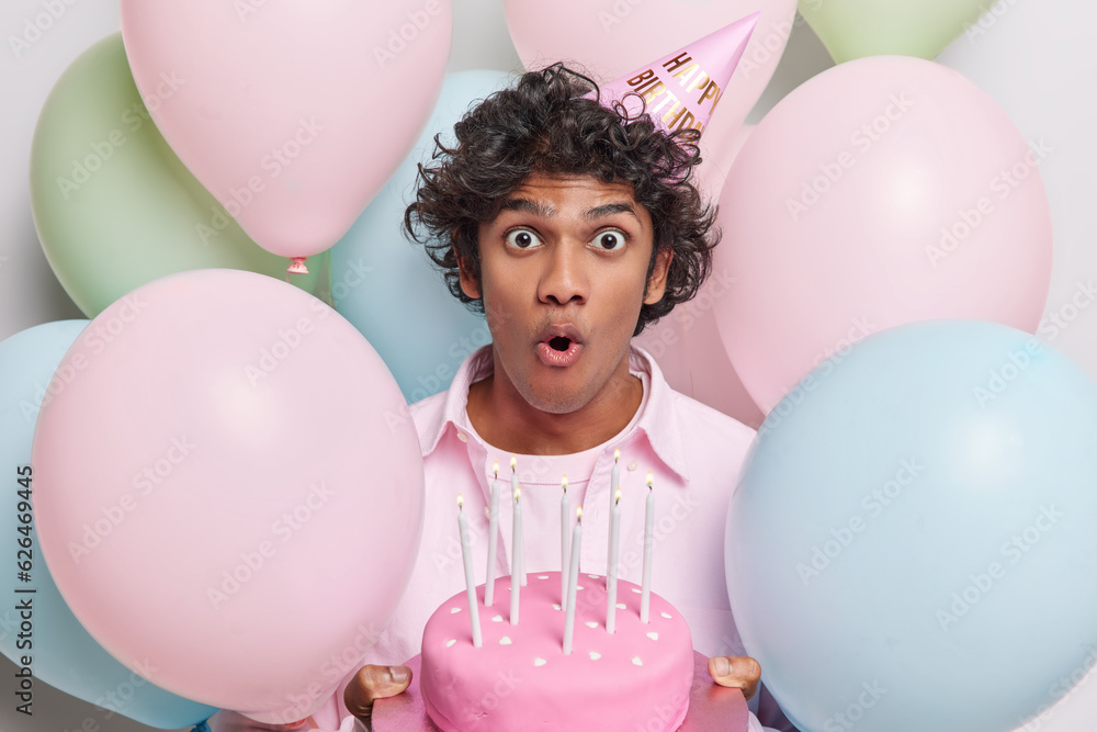Shocked curly haired man poses with festive cake makes every moment ...