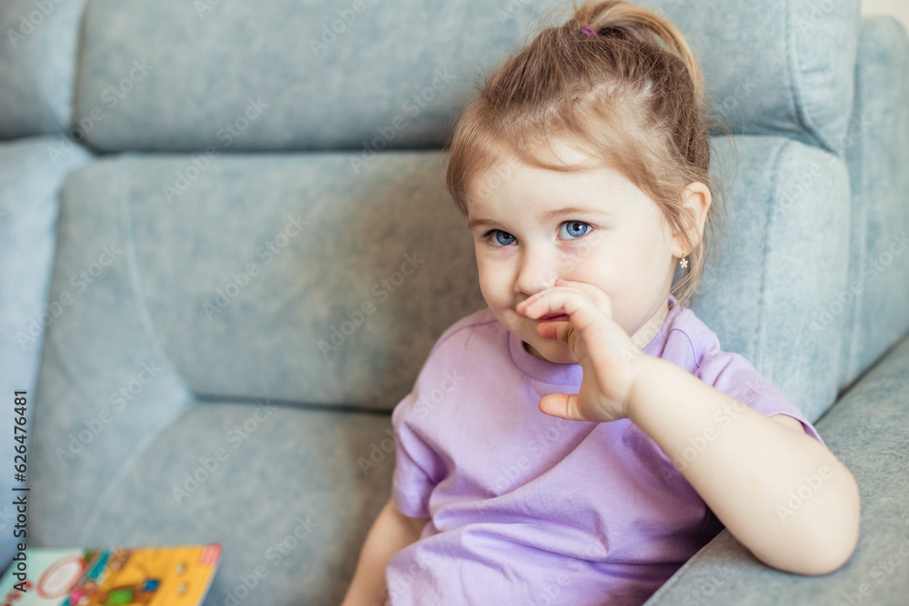 Portrait of cute little girl with blue eyes, smiling, looking at the camera sitting on the couch at home, copy space Portrait of cute little girl with blue eyes, smiling, looking at the camera sitting on the couch at home, copy space