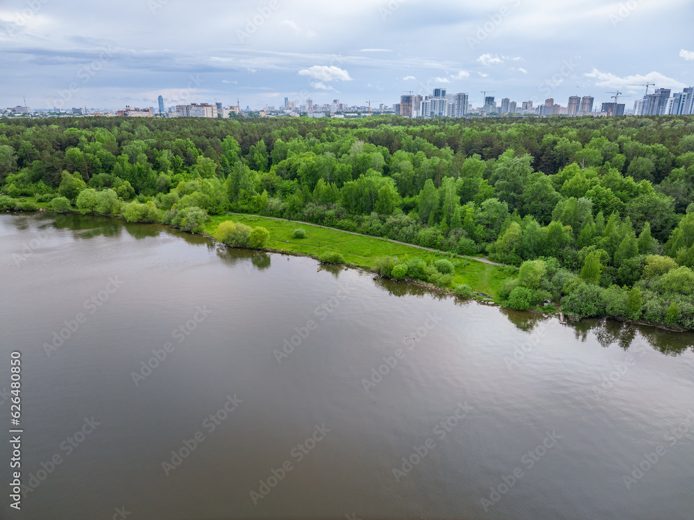 Big lake with green shores in bright sun light and city on horizon, aerial landscape. Recreation concept. Aerial view