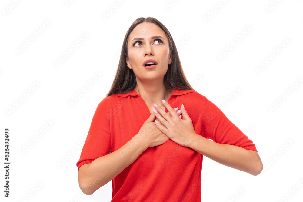 young charming european woman with black hair dressed in a red t-shirt looks up in surprise on a white background young charming european woman with black hair dressed in a red t-shirt looks up in surprise on a white background