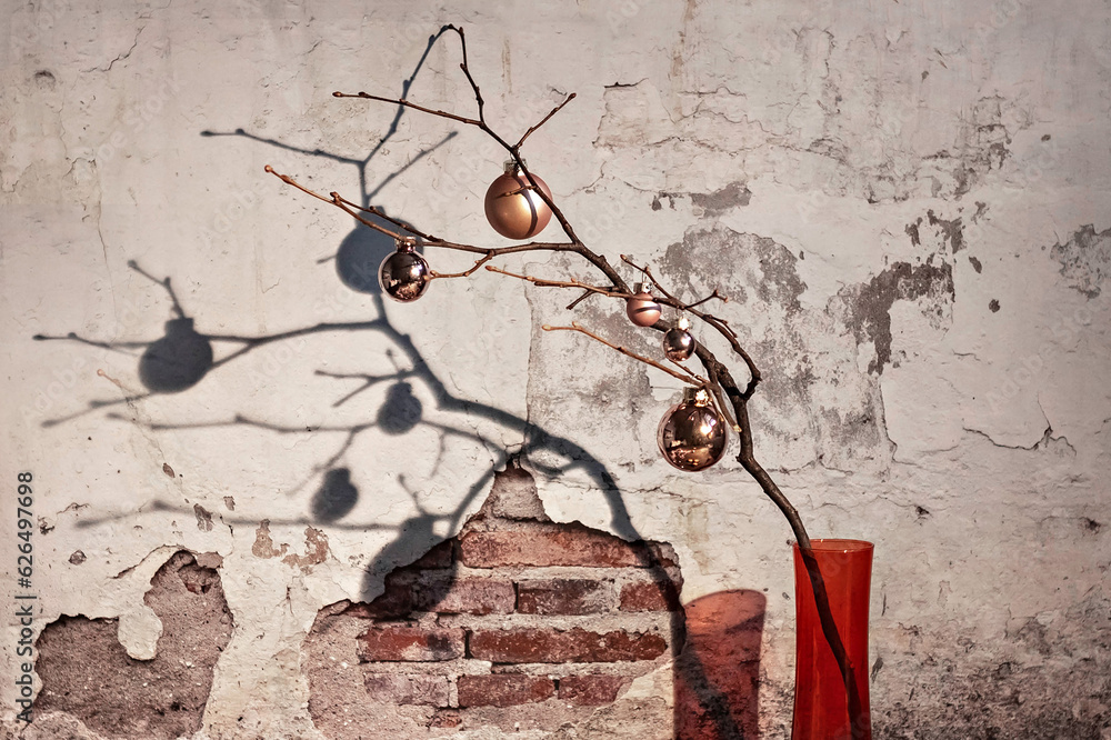 Fototapeta premium Christmas balls on dry tree branches, which stand in a vase against the background of an old vintage brick wall with cracked plaster on the background of the texture of plaster. retro Grunge.