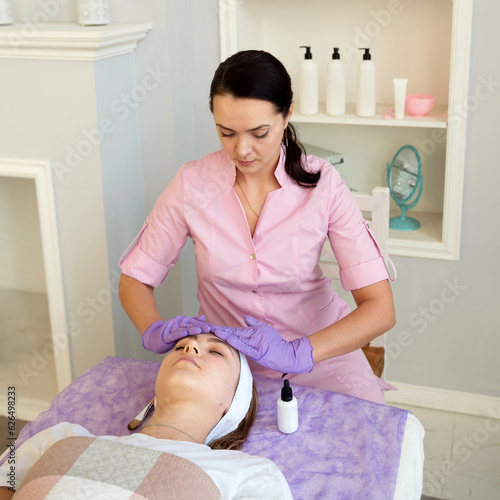 people, beauty, spa, cosmetology and skincare concept - happy young woman with closed eyes getting face massage at spa salon