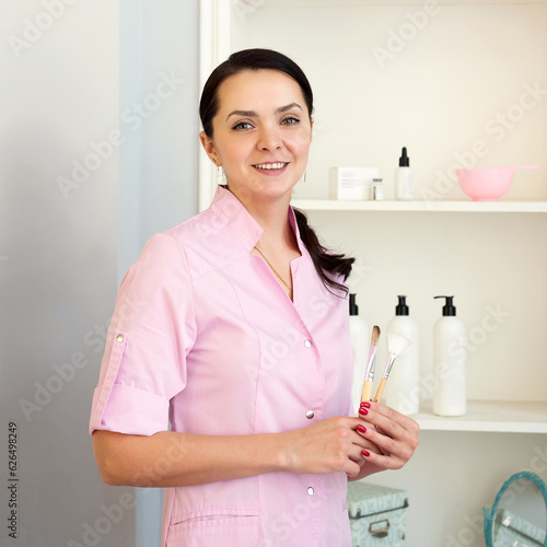 Smiling female cosmetologist with brushes in her hands looking at camera
