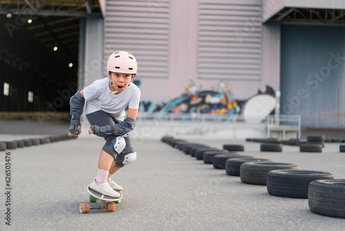 asian child skater or kid girl fun playing skateboard or enjoy riding carving surf skate on car tires track in skatepark lane for extreme sports exercise and wears helmet knee guard for body safety