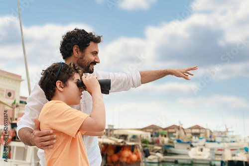 Father and Son Using Binoculars on a Yacht - A Caucasian father helps his son to use binoculars on a small yacht, looking at something afar.